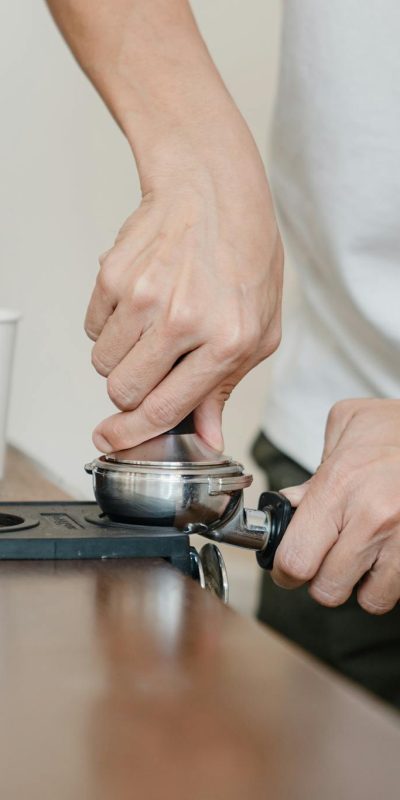 Crop barista preparing coffee pod in holder with tamper