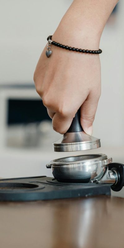 Crop barista working with tamper and coffee machine holder